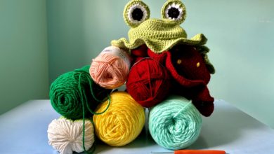 Two crocheted hats rest on top of a multicoloured pile of yarn.