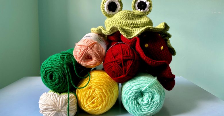 Two crocheted hats rest on top of a multicoloured pile of yarn.