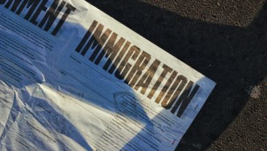 A newspaper with "IMMIGRATION" in large blocked letters lies on the pavement.