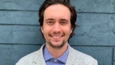 Young man in grey suit standing in front of blue wall