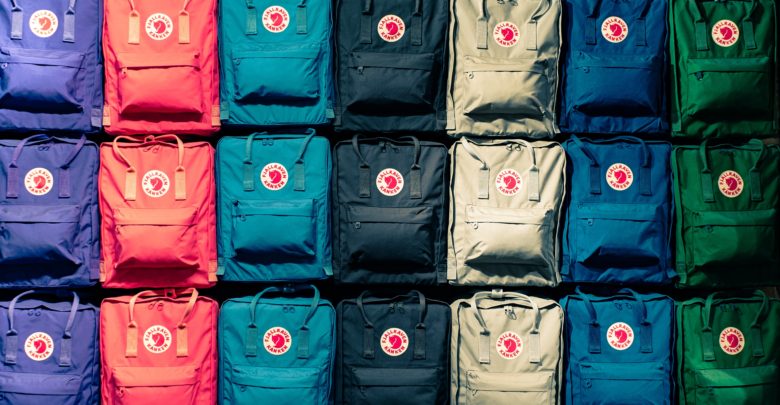 A photo of Fjällräven backpacks on a wall lined up by colour. These are a common type of school bag.