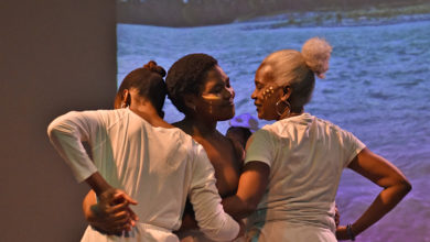 Three dancers stand in front of a screen for Site/Sight/Place.