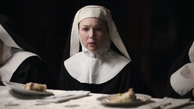 Sister Agnes sits at a table beside two other sisters with dinner in front of them. She looks at the camera with a disturbed face.