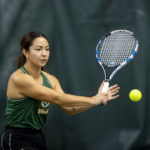 A Panda tennis player in uniform swings a tennis racquet at a tennis ball.
