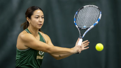 A Panda tennis player in uniform swings a tennis racquet at a tennis ball.