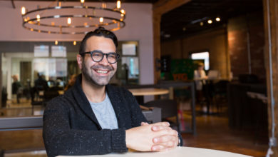 Omar Mouallem sits smiling with his hands folded on a table.