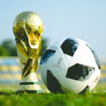 The 2018 FIFA soccer trophy sits next to a soccer ball on a field