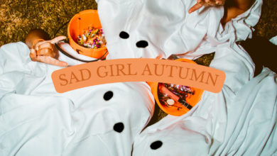 Three people wearing ghost costumes lay on the grass next to their Halloween haul. The text "Sad girl autumn" is placed in the middle of the graphic.