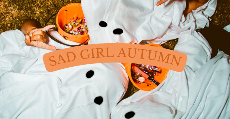 Three people wearing ghost costumes lay on the grass next to their Halloween haul. The text "Sad girl autumn" is placed in the middle of the graphic.
