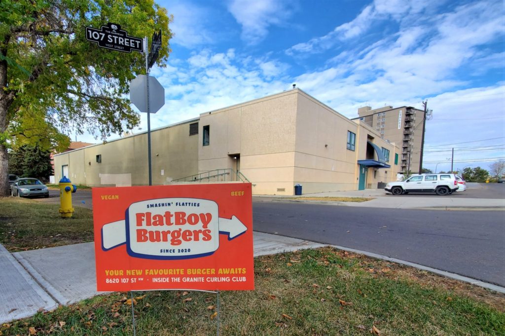 The Flat Boy Burgers sign pointing towards the exterior of the Granite Curling Rink