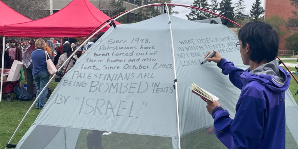 student writes on tent at sit in